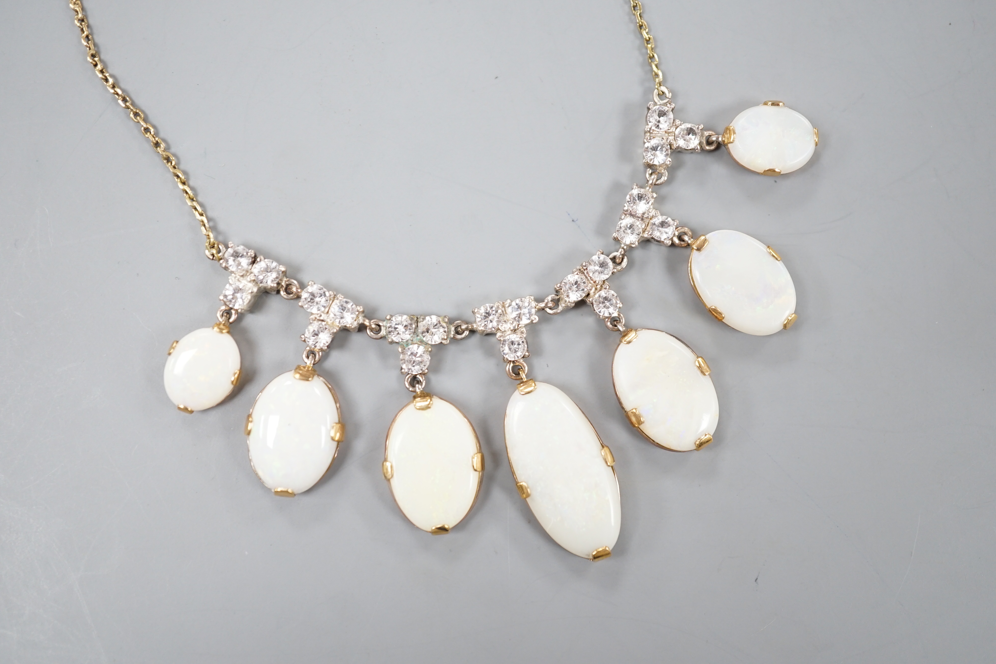 A yellow metal, graduated seven stone oval white opal and paste set cluster fringe necklace, 42cm, gross 14.6 grams.